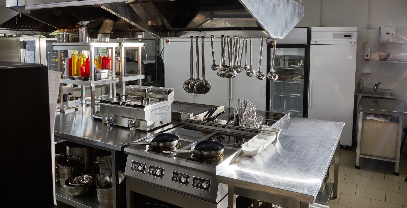 Stainless steel commercial kitchen in the UK with a gas cooking range, fryers and extraction canopy