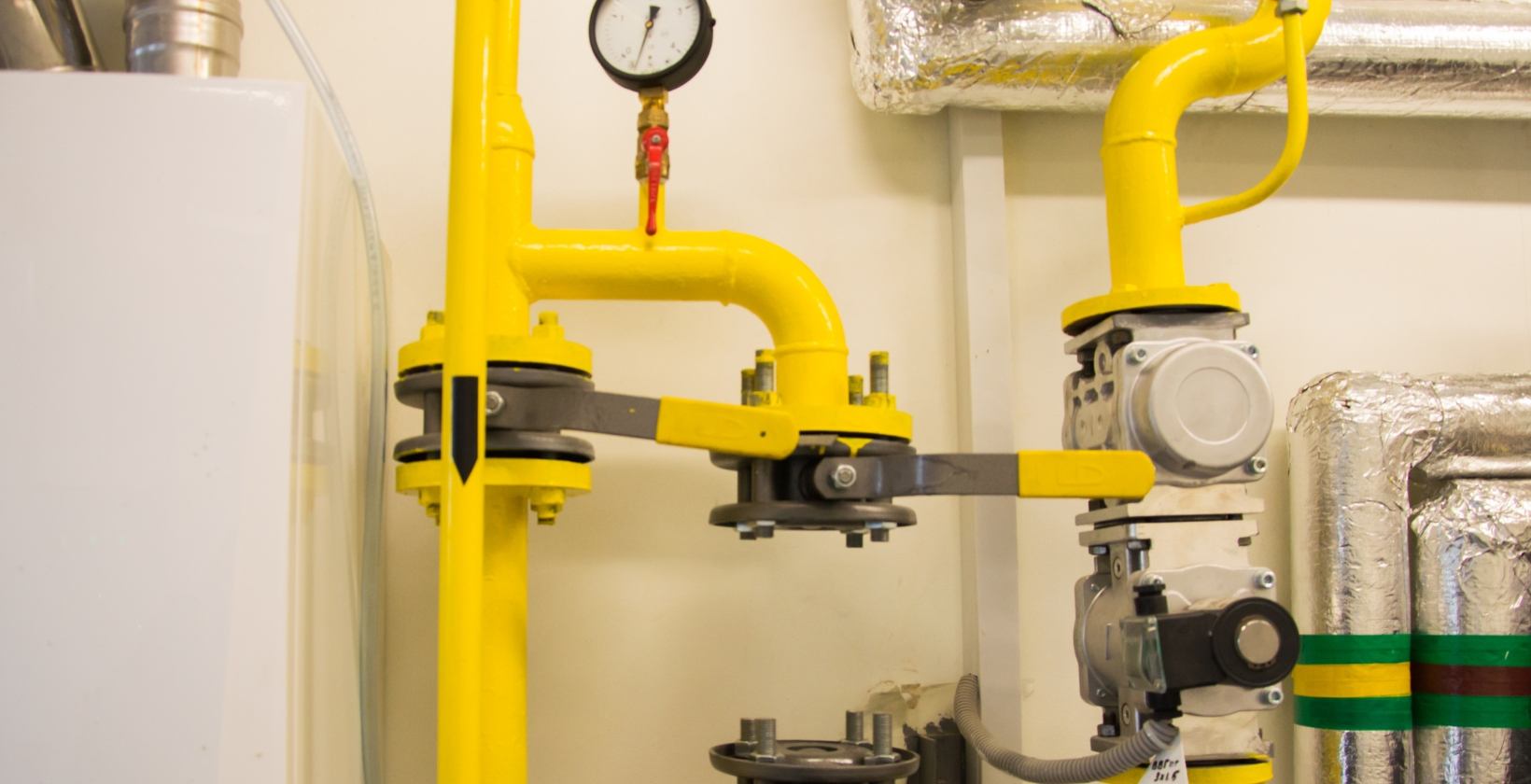 Commercial gas installation in a UK plant room: yellow gas pipework with a pressure gauge, flanged isolation valves and a gas train