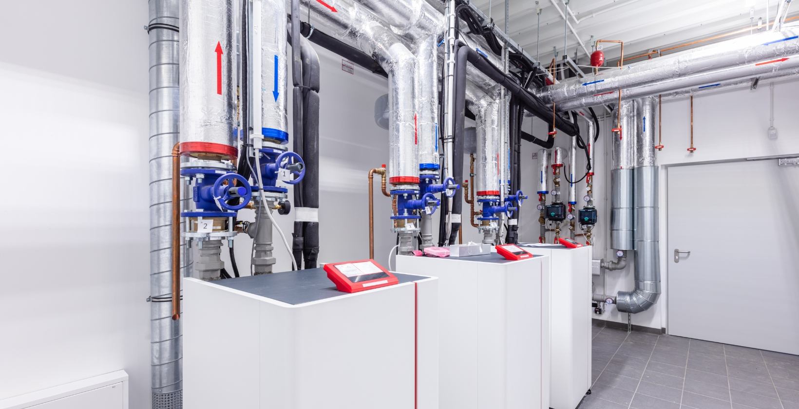UK commercial plant room with floor-standing gas boilers, insulated flow and return pipework and blue isolation valves