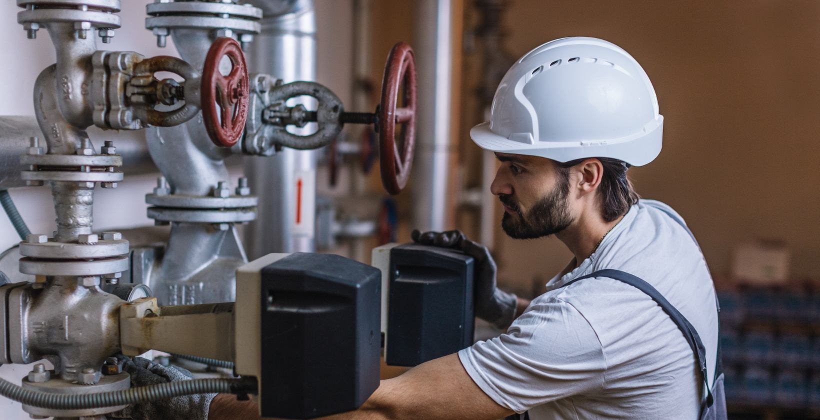 Gas engineer in a white hard hat checking valves and gauges on commercial gas pipework during a tightness test in the UK