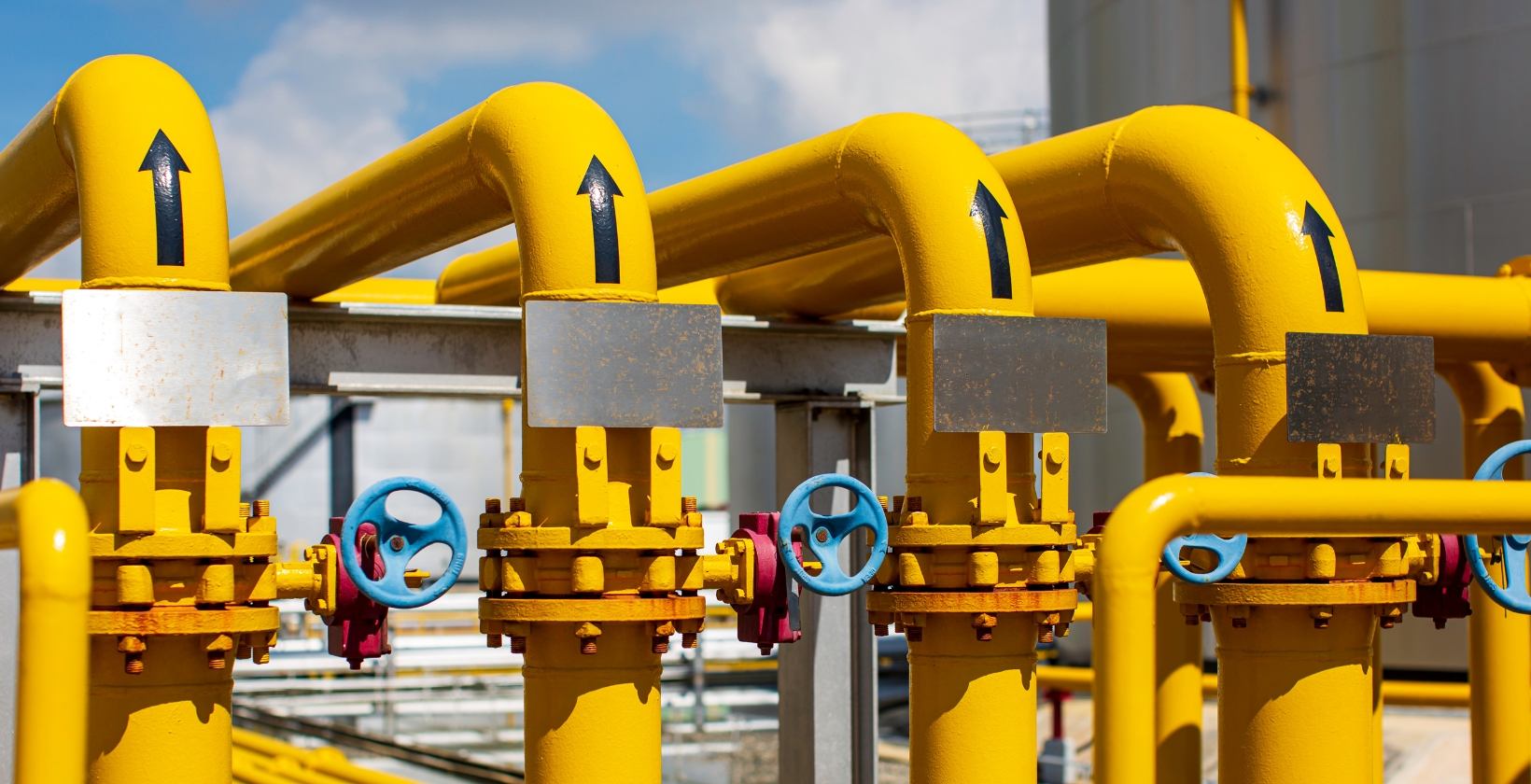 Commercial and industrial gas services UK Yellow industrial gas pipelines with flow arrows and blue handwheel valves at a UK industrial gas installation